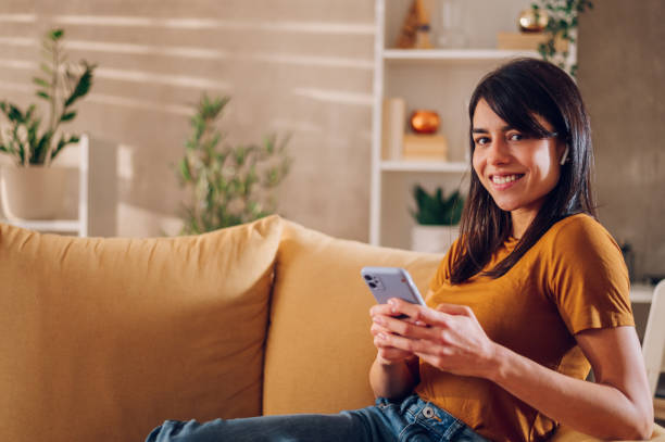istock Beautiful woman using smartphone while relaxing on the sofa at home 1478683199