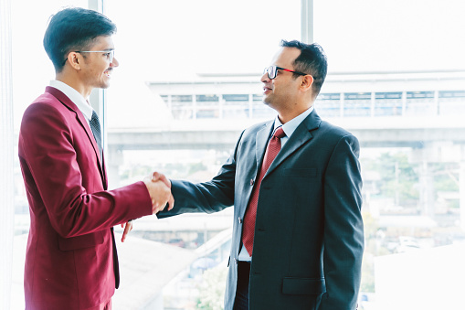 Two smiling businessmen shaking hands while standing in an office.