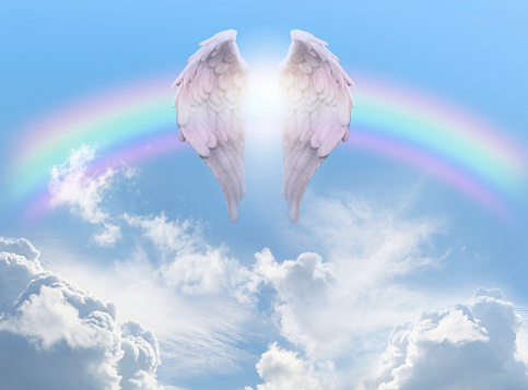 pair of angel wings infront of a rainbow arc against a beautiful blue sky with fluffy clouds ideal for a spiritual or religious blessing theme