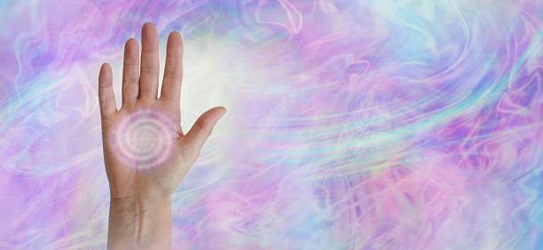 female hand facing outwards with a pink spiralling vortex energy formation in the palm against a wide pink blue purple misty ethereal energy field