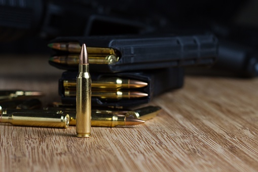 A single .223 bullet, standing in front of loose ammo and two AR-15 magazines loaded with ammunition