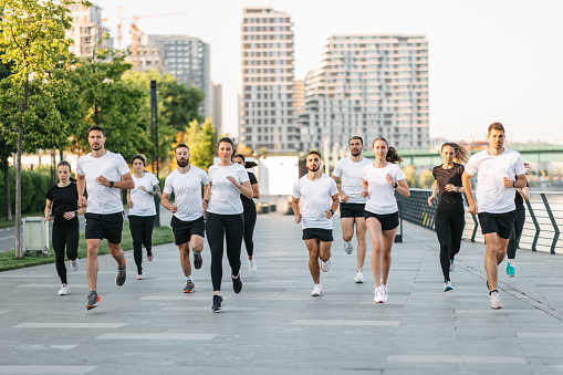 Team of athletic young people running through the city park in Belgrade Waterfront. Running clubs preparing for half-marathons. People from the club running in the morning before the high temperature