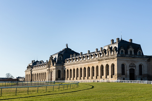 Chantilly, France - February 24, 2023: Late afternoon shot of the Royal Stables of Château de Chantilly with the racecourse in the foreground.