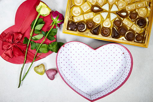 chocolate pieces from various type in box for valentine's day with open red heart shaped box and roses flowers