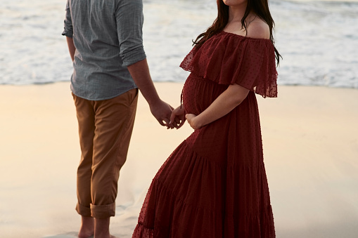 Pregnant, outdoor and couple at beach holding hands with love for maternity and relationship. Man and woman together in nature for travel vacation in summer for healthy pregnancy, support and romance