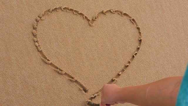 Girl drawing heart on sand with a stick.