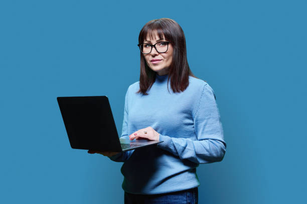istock Serious mature woman using laptop looking at camera on blue background 1478714421