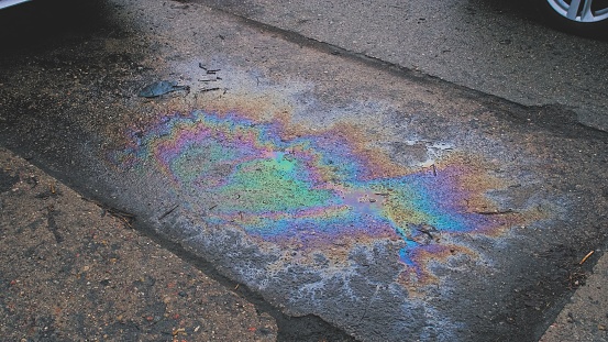 Toxic Colorful Spilled Gasoline Stain Smudges on Rough Wet Surface of Parking Lot Pavement