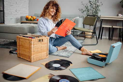 Woman looks at old gramophone records while sitting in the living room of her apartment