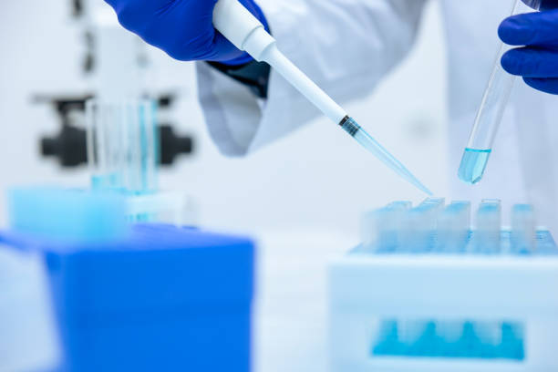 istock Unrecognizable scientist dripping blue liquid from pipette into test tube at table in laboratory. 1478718605