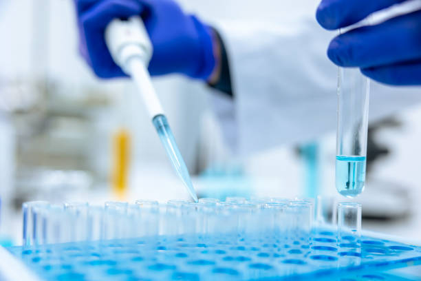 istock Unrecognizable scientist dripping blue liquid from pipette into test tube at table in laboratory. 1478718616