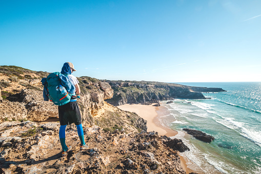 Passionate young backpacker tracks rocky cliffs on the Atlantic coast near Vila Nova de Milfontes, Odemira, Portugal. In the footsteps of Rota Vicentina. Fisherman trail
