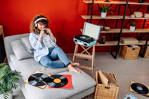 Woman is sitting on a sofa and listening to music on a record player