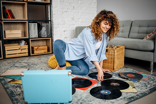 Woman looks at old gramophone records while sitting in the living room of her apartment
