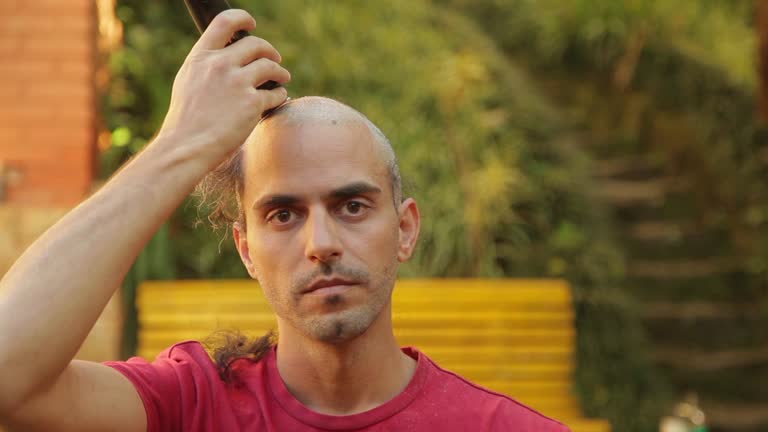 Portrait of young man shaves his head with machine. Head with dandruff. Buzzing His Own Hair.