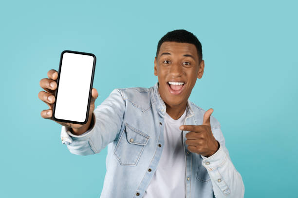 istock Wow, cool website. Satisfied young african american guy pointing finger at smartphone with empty screen 1478730391