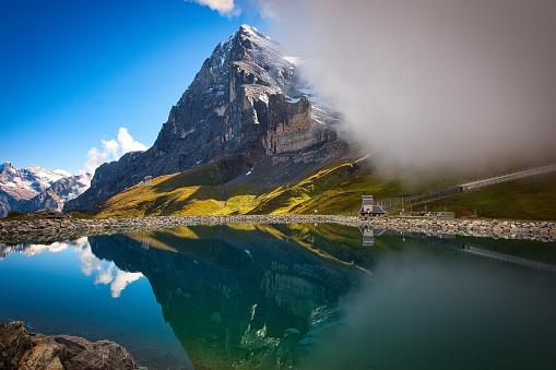 A scenic shot of Eiger Mountain reflecting on a small lake under a blue sky in Switzerland