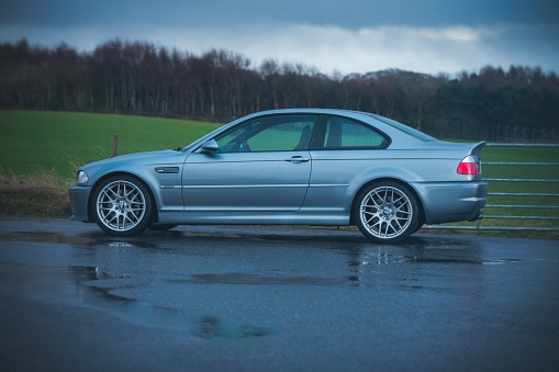 Inverness, United Kingdom – January 29, 2022: The view of a gray BMW M3 CSL parked on the wet asphalt before a field