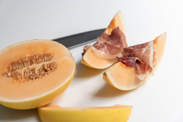 Two melon slices with cured ham slices on top with a half melon and knife