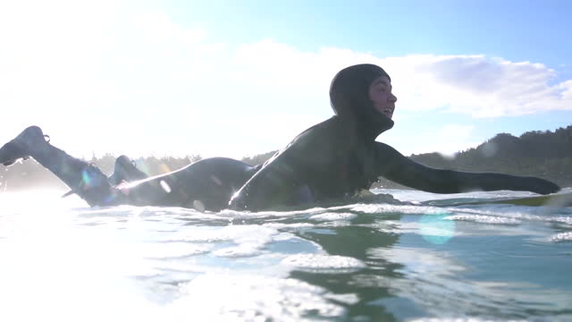 Young woman paddles out into surf