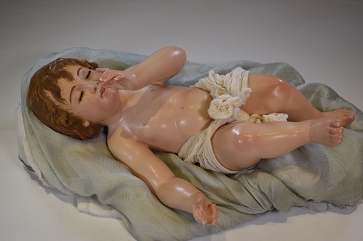 A high-angle shot of a statue of a Holy Child lying on a cloth on a bed - baby from The Nativity during Christmas Season