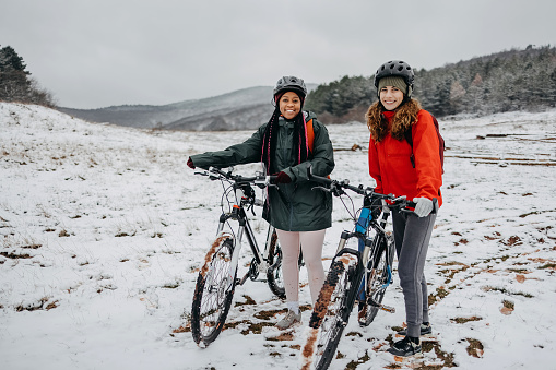 Portrait of two women standing next to their bicycles on a snowy mountain