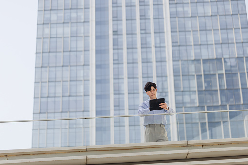 The photo was taken at 122 Huayuan Road, Zhengzhou, China.This is a shopping mall called Triumph Square.Not a famous building.\n\nAn Asian young man wearing casual clothes. He is a business person who uses a digital tablet in  scene in the city.