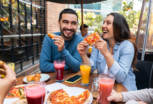 Happy couple having fun eating pizza at a restaurant with a group of friends and laughing