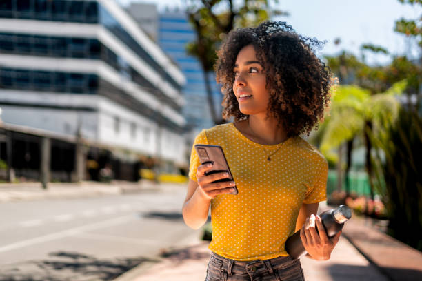 młoda kobieta idąca ulicą za pomocą telefonu komórkowego - young adult lifestyles city life drinking zdjęcia i obrazy z banku zdjęć