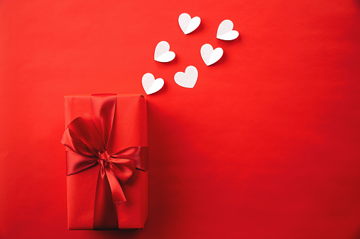 A top view of red gift box with ribbon and hearts isolated on a red background