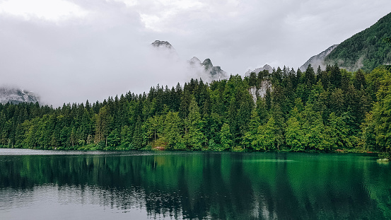 A landscape of a lake surrounded by forests covered in the fog under a cloudy sky