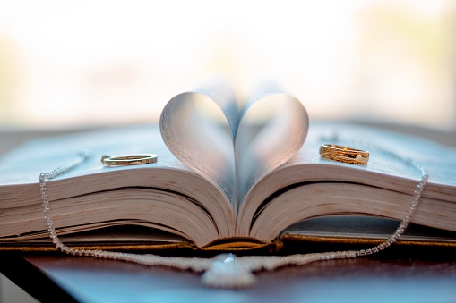 A heart made of the pages of a book with the marriage rings on both sides