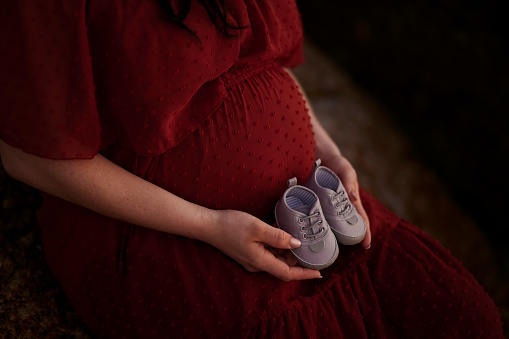 Photoshoot, expecting and a pregnant woman holding shoes for a photo, maternity reveal and a memory. Cute, model and a mother with boots of a baby during a pregnancy shoot, filming or picture