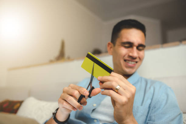 はさみでクレジットカードを切るヒスパニック系の若い男性 – ホームバンキングとテクノロジーのコンセプト - home finances cutting scissors finance ストックフォトと画像