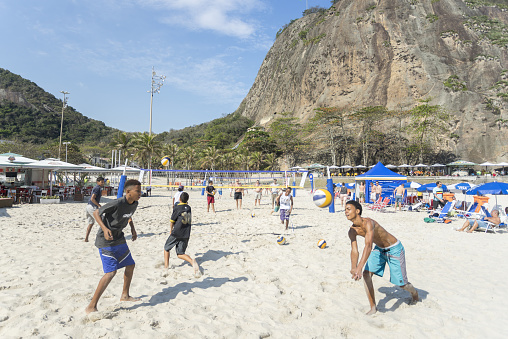 Rio de Janeiro, Brazil – August 16, 2016: Adolescent boys playing volleyball on the beach of Copacabana with the Leme hill in the background on a bright sunny day