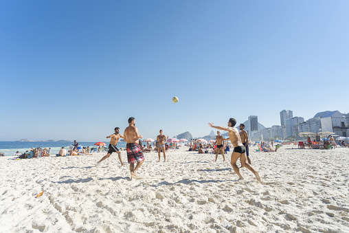 Rio de Janeiro, Brazil – August 14, 2016: Youngsters playing foot volley on the beach of Copacabana on a bright sunny day with blue sky with typical neighbourhood scenery in the back