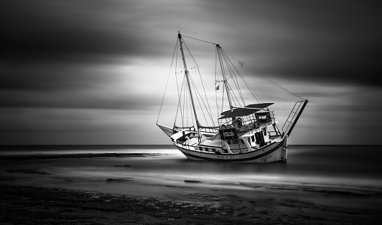 A grayscale of a yacht moored at a beach on a gloomy day shot in long exposure