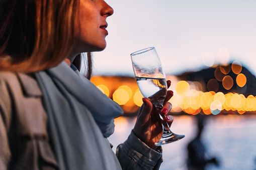 A girl with a scarf on her neck holds a glass of drink. the lower half of the face. blurred the lights of the evening city