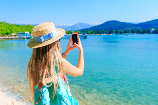 Back view of a woman with the phone in hand and do photos. beautiful lake and mountains on the background