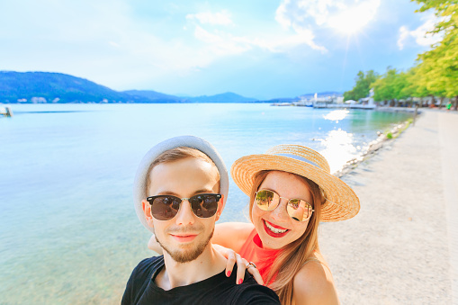 Young happy couple in mountain lake making selfie photo. a guy with a beard in sunglasses and boater. girl in sunglasses and boater