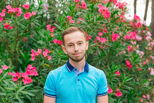a guy with a beard in polo looking into the camera on the background of bushes with flowers