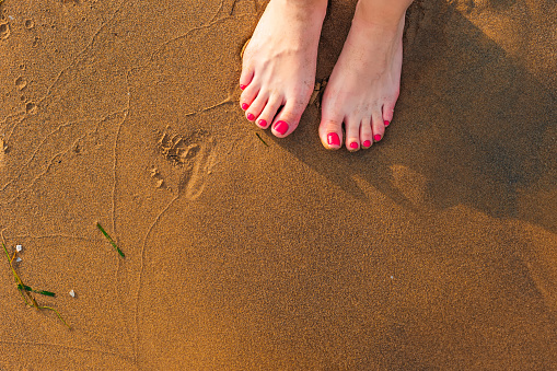 Low section view of a young woman legs standing on sand on the beach. Shadows of feet on sand