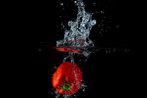 A closeup view of colorful bell peppers dropped into water creating a splash on a black background