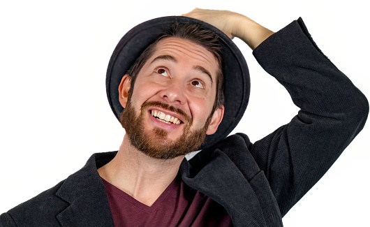 The portrait of handsome man with beard in fedora hat and blazer looking up and smiling on white background