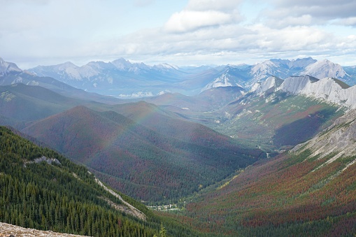 A beautiful rainbow appearing over a vast mountain landscape in Alberta, Canada.