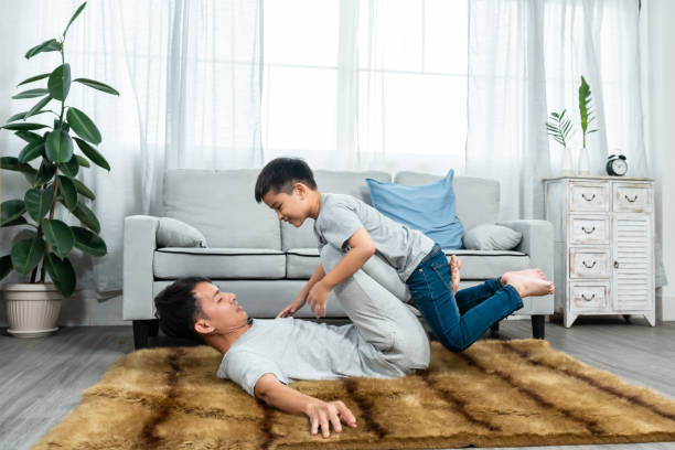 papa dormait sur la moquette, couvrant le sol de la chambre, levait les jambes, faisait asseoir le fils sur ses jambes, levait les jambes quand le fils s’asseyait faisait monter le motif, le fils levait les bras, jouant joyeusement avec son père. - torso physical therapy patient relaxation exercise photos et images de collection