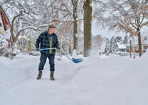 A Caucasian man shoveling sidewalk in the morning. The image was taken after a few days of the worst snow storm in decades, covering the whole city with snow. The road was empty in the morning and the location of the photo was Saint Paul, Minnesota.