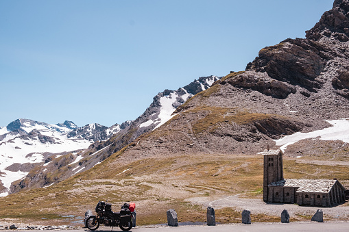 A sunny spring day in the French Alps where motorcyclists parked their bikes by the side of the road.  This is the highest point along the Col de L'Iseran ( 2770 m). Rugged mountain landscape with snow and a chapel built of rough stone. Popular area for cyclists, motorcyclists and road trips by car.