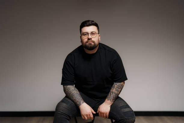 Calm bearded and tattooed man sitting on chair in studio
