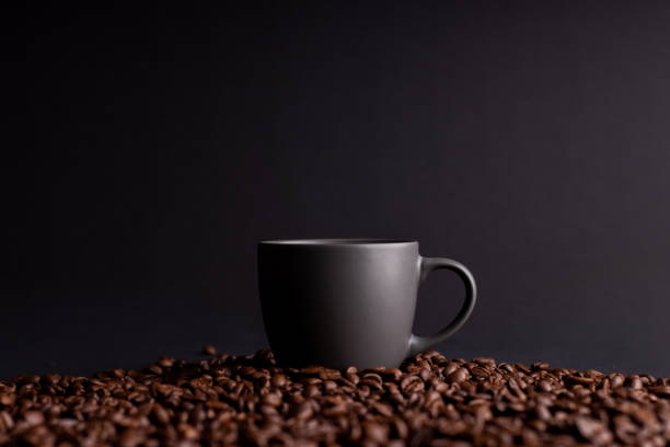 a coffee mug among coffee beans, black isolated background